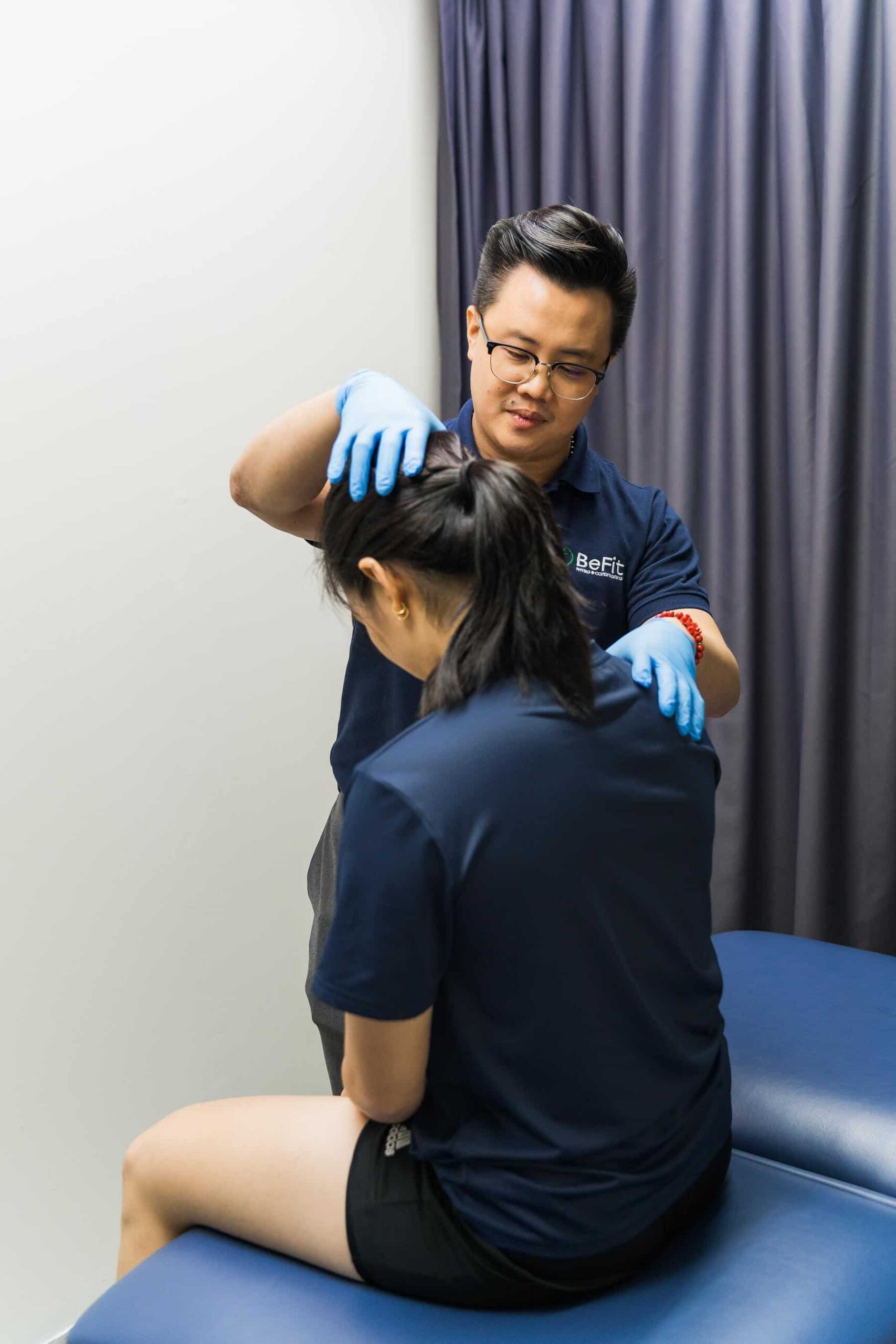Physiotherapist performing neck and shoulder manual therapy on seated patient using palpation and massage techniques. Shows cervical treatment, upper body therapy, posture correction, and hands-on assessment. Keywords: neck treatment, shoulder therapy, manual palpation, cervical spine, posture assessment, upper body rehabilitation.