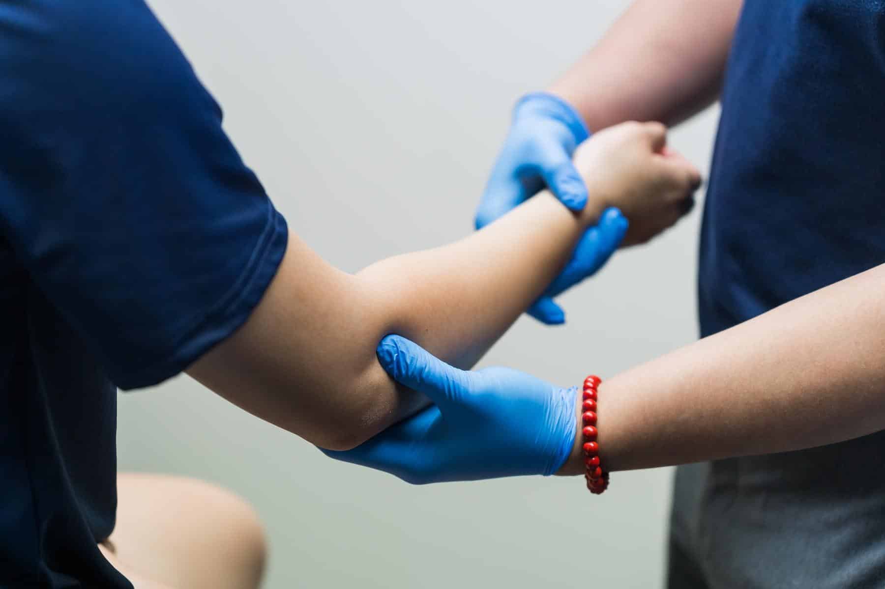 Close-up manual palpation and examination of patient's arm and wrist by physiotherapist using therapeutic touch. Shows detailed assessment, joint evaluation, tissue examination, and diagnostic technique. Keywords: arm examination, wrist assessment, manual palpation, joint evaluation, physical examination, diagnostic therapy.