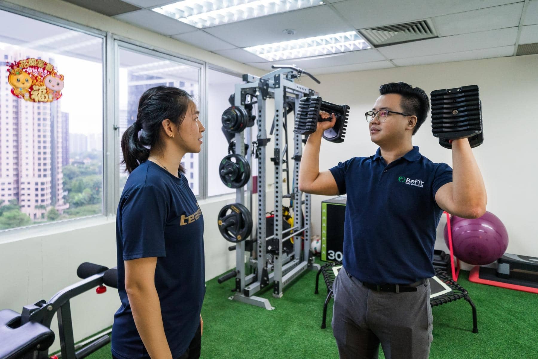 Two physiotherapists demonstrating dumbbell exercise and strength training with modern equipment in clinic gym. Shows resistance training, weight-based rehabilitation, fitness coaching, and exercise guidance in professional facility. Keywords: strength training, dumbbells, exercise program, resistance therapy, fitness coaching, gym equipment.